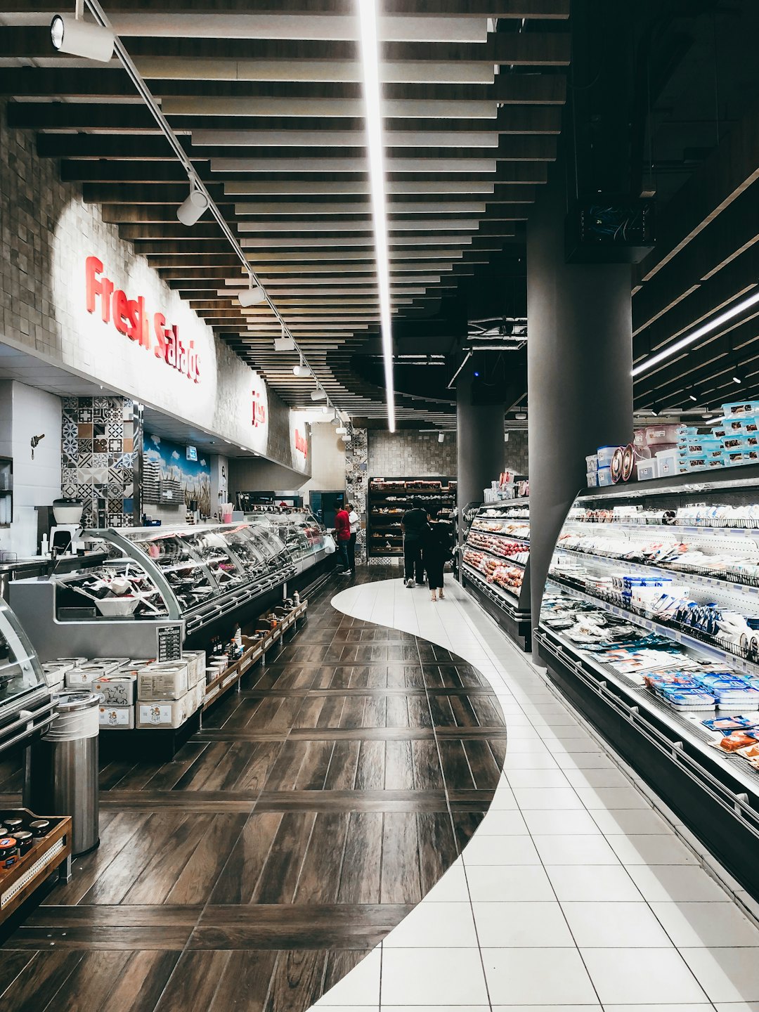Şarküteri ve paketlenmiş gıdaların bulunduğu modern bir markette alışveriş yapan müşteriler.