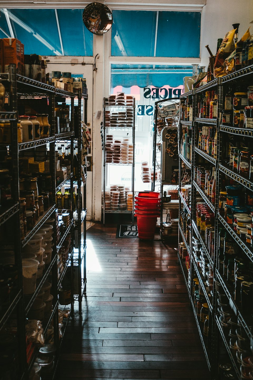 Ürünlerle dolu, aydınlık bir girişe doğru giden dar market koridoru.