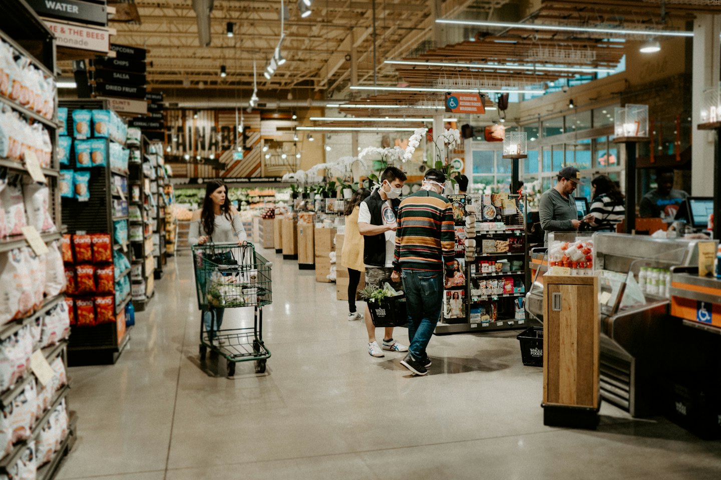 Maskeli bir adamın modern bir markette birileriyle konuştuğu an.